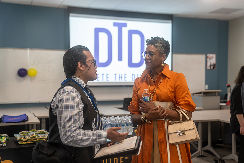 Man and lady talking in front of a projection of the Delete the Divide logo